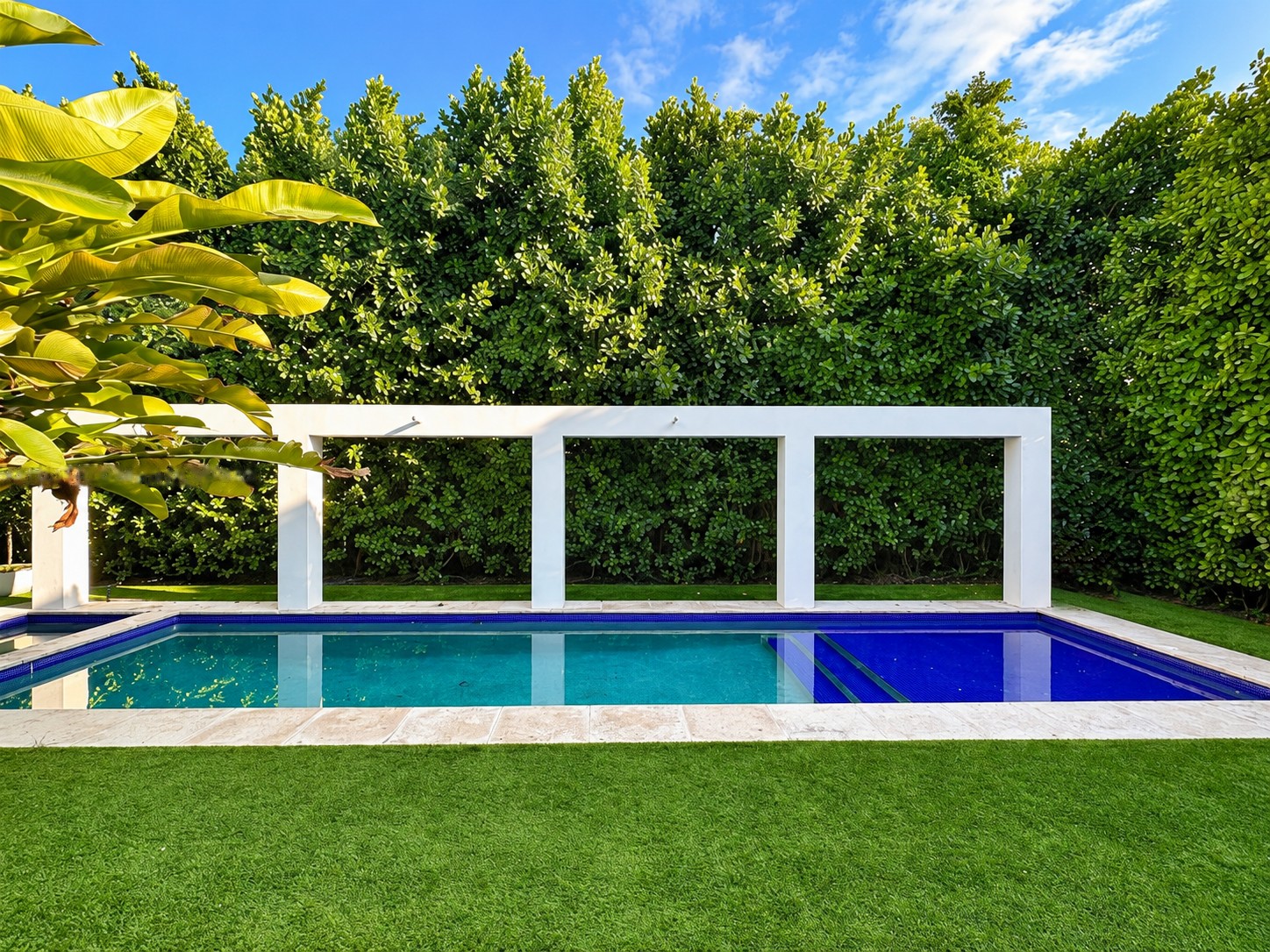 The Rivo Alto Island house pool, cobalt tiled steps beneath a white pergola against a tall clipped hedge