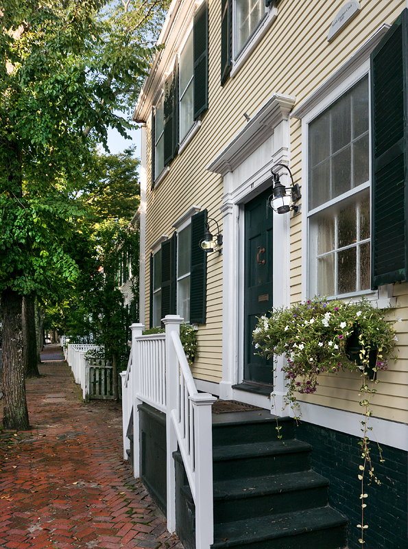 The front door and window box from the brick sidewalk, with the picket fence running down the street