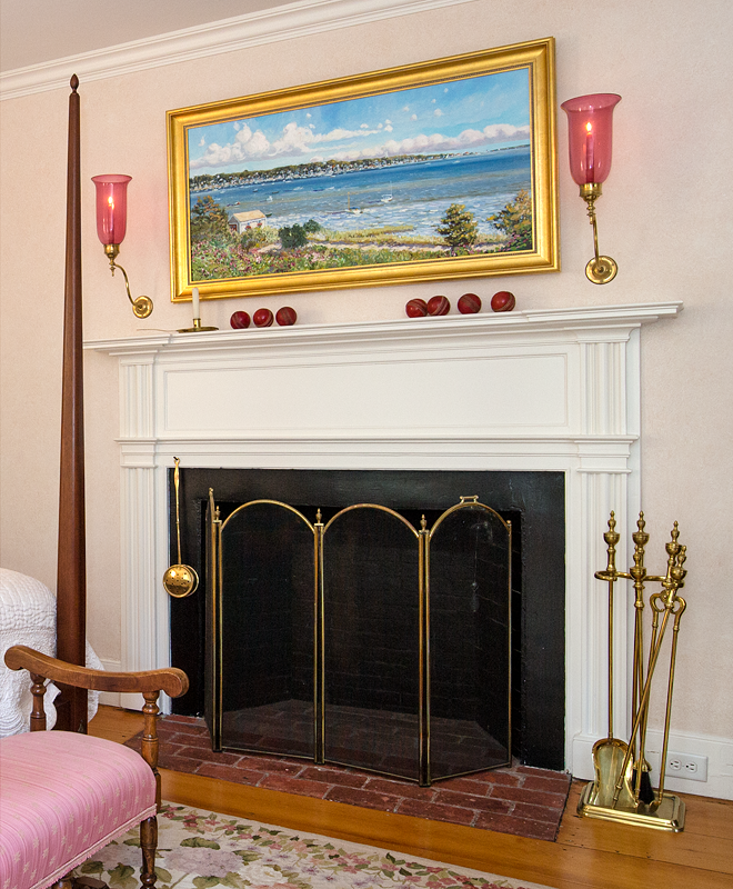 Mantel with a harbour painting, cranberry glass sconces and small apples along the shelf