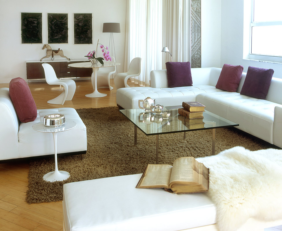 Living room with long white tufted leather seating, aubergine and wine cushions and a glass and steel table