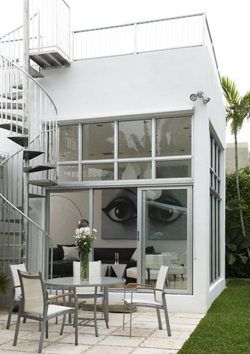 The Rivo Alto Island house from the garden, a steel spiral stair to the roof deck and a terrace table on palm shaded paving